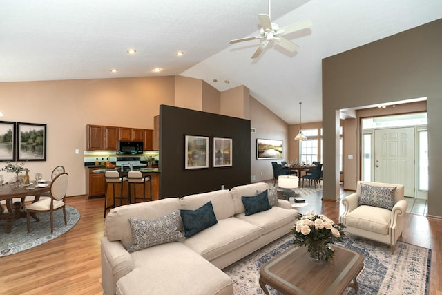 living room with ceiling fan, high vaulted ceiling, and light wood-type flooring