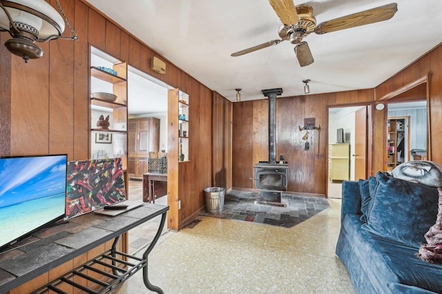 living room with ceiling fan, wood walls, and a wood stove