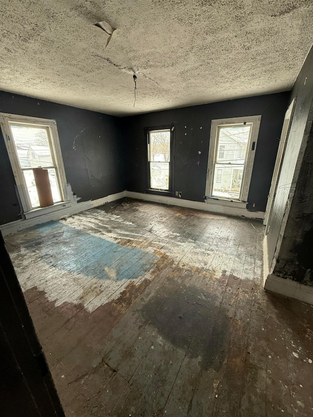 spare room featuring a healthy amount of sunlight, a textured ceiling, and hardwood / wood-style flooring