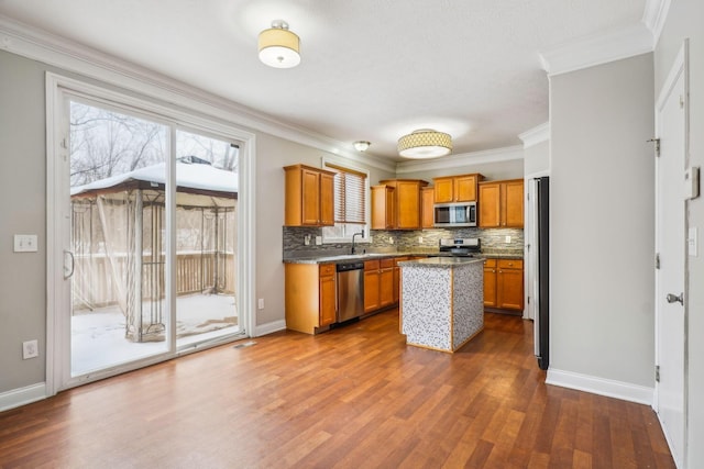 kitchen featuring tasteful backsplash, ornamental molding, stainless steel appliances, sink, and a kitchen island