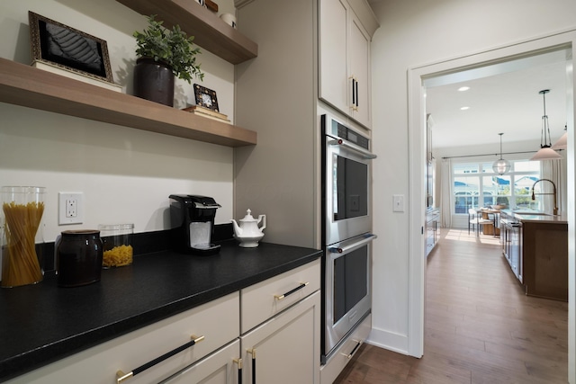 kitchen featuring stainless steel double oven, dark wood-type flooring, sink, pendant lighting, and white cabinets