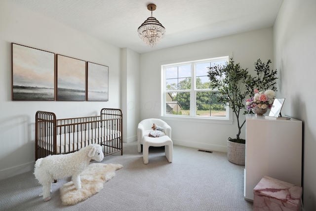 bedroom featuring a crib, carpet flooring, and a notable chandelier