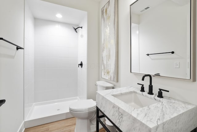 bathroom with hardwood / wood-style floors, toilet, sink, and a tile shower