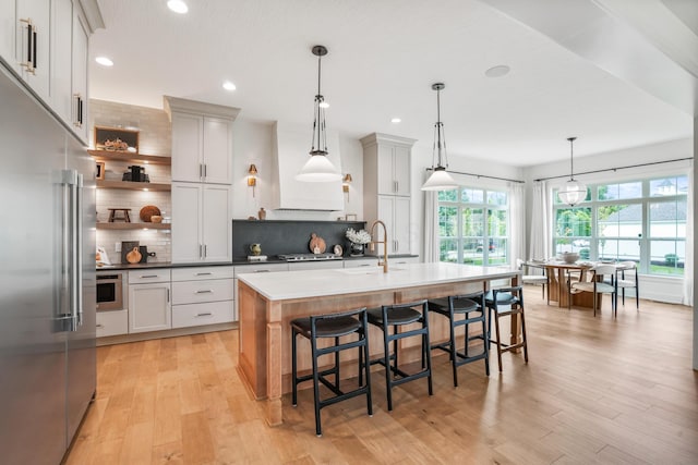 kitchen with light hardwood / wood-style flooring, an island with sink, tasteful backsplash, decorative light fixtures, and stainless steel appliances