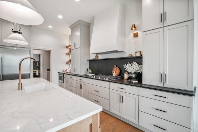 kitchen with sink, dark stone counters, decorative light fixtures, and custom exhaust hood