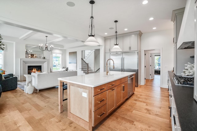 kitchen featuring pendant lighting, premium range hood, an island with sink, beam ceiling, and stainless steel appliances