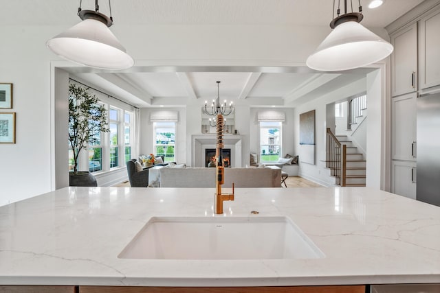 kitchen featuring a center island with sink, gray cabinets, light stone countertops, and hanging light fixtures