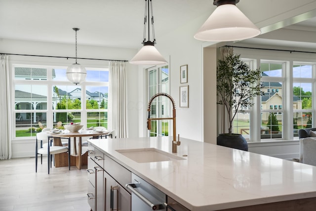 kitchen featuring light stone countertops, sink, an island with sink, and hanging light fixtures