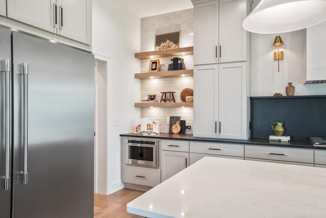 kitchen featuring decorative backsplash, light hardwood / wood-style floors, high quality fridge, and dark stone counters