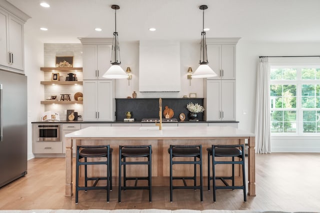 kitchen with a breakfast bar, a kitchen island with sink, hanging light fixtures, decorative backsplash, and appliances with stainless steel finishes