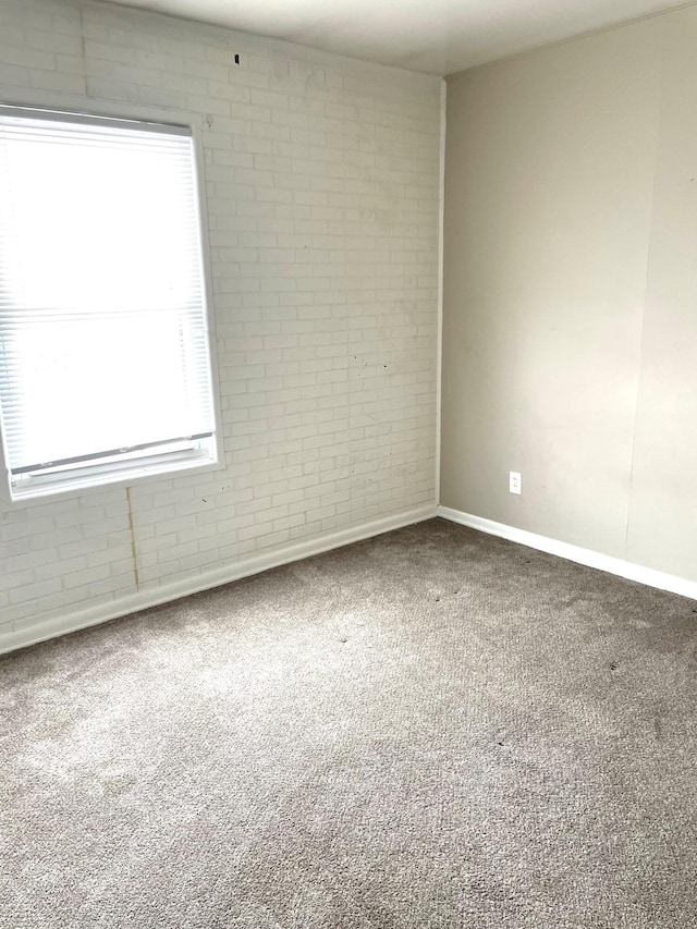 carpeted spare room featuring brick wall