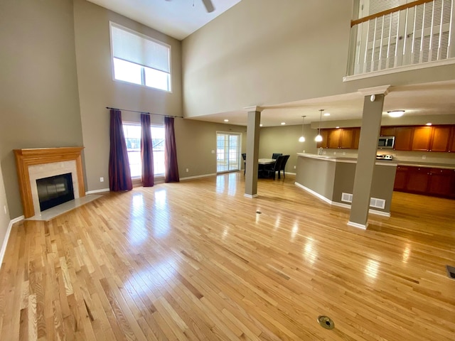 unfurnished living room with a high end fireplace, a high ceiling, light wood-type flooring, and ceiling fan