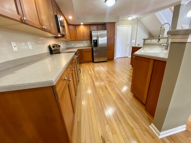 kitchen with backsplash, sink, stainless steel appliances, and light hardwood / wood-style flooring