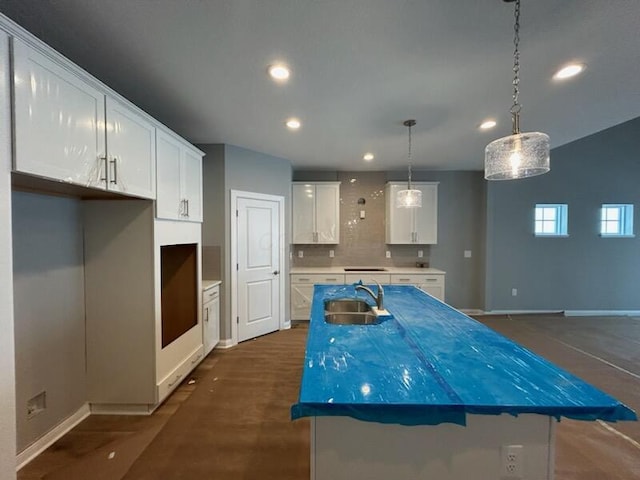 kitchen featuring tasteful backsplash, sink, a center island with sink, white cabinetry, and hanging light fixtures