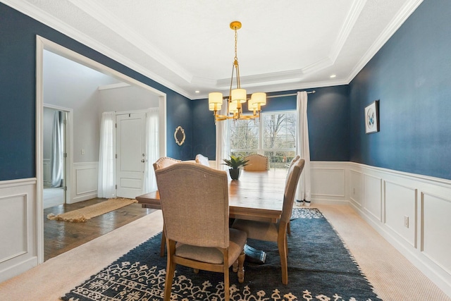 dining room with a raised ceiling, crown molding, light colored carpet, and a notable chandelier