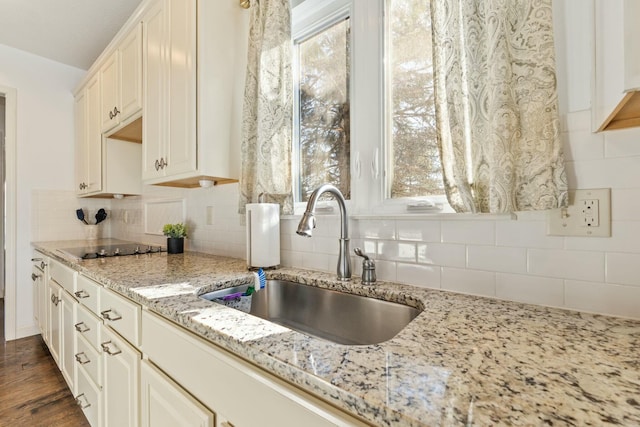 kitchen with dark wood-type flooring, sink, black electric cooktop, light stone countertops, and decorative backsplash