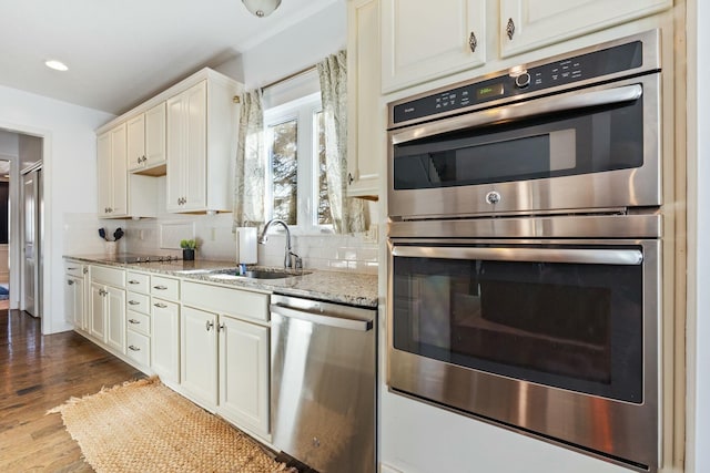 kitchen with sink, backsplash, stainless steel appliances, light stone countertops, and dark wood-type flooring