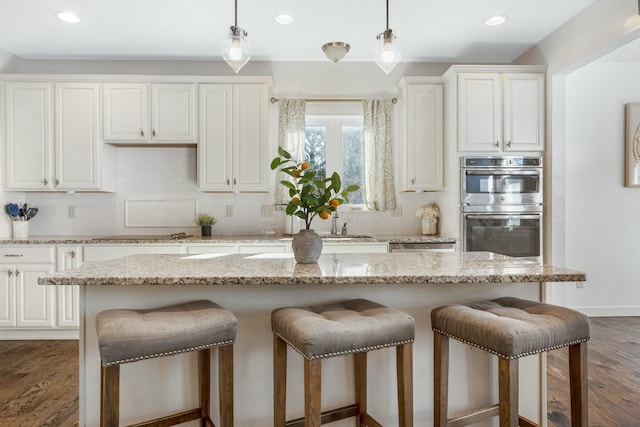 kitchen with dark wood-type flooring, light stone counters, a center island, double oven, and white cabinets