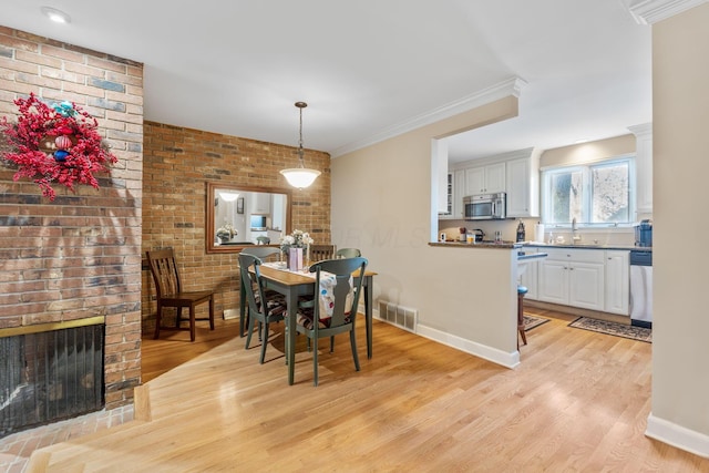 dining area featuring sink, a brick fireplace, light hardwood / wood-style flooring, brick wall, and crown molding