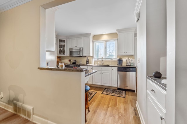 kitchen featuring kitchen peninsula, light wood-type flooring, stainless steel appliances, sink, and white cabinets