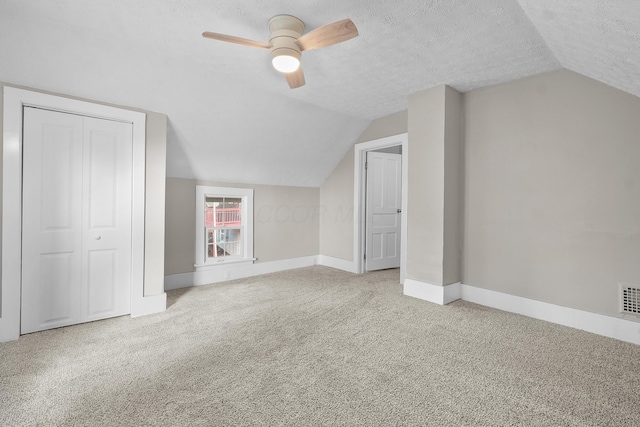 additional living space with a textured ceiling, ceiling fan, light carpet, and vaulted ceiling