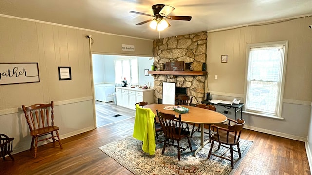 dining area with a stone fireplace, crown molding, hardwood / wood-style floors, and ceiling fan