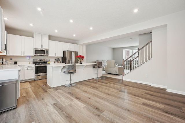 kitchen with light wood-type flooring, stainless steel appliances, white cabinets, a kitchen island, and a breakfast bar area