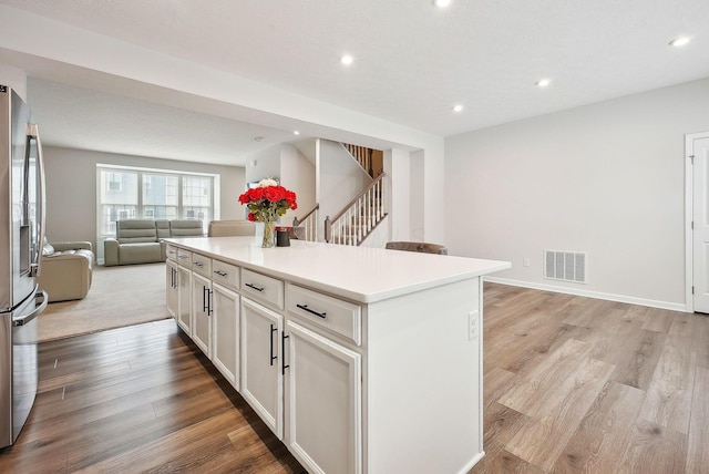 kitchen with stainless steel fridge, a center island, light wood-type flooring, and white cabinetry