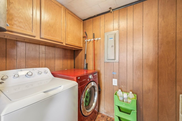 laundry room featuring wooden walls, washer and dryer, cabinets, and electric panel