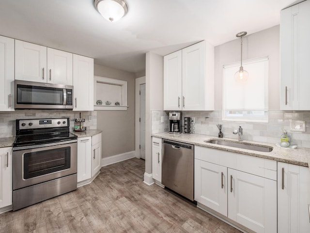 kitchen with white cabinets, stainless steel appliances, light hardwood / wood-style floors, sink, and hanging light fixtures