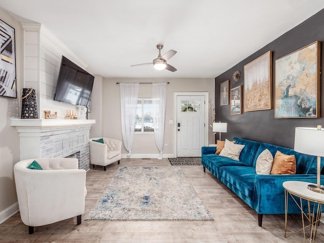 living room featuring ceiling fan, a brick fireplace, and light hardwood / wood-style floors