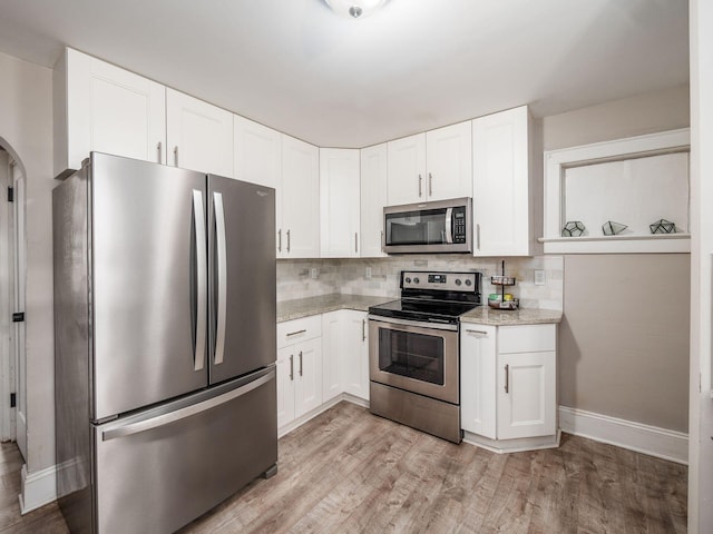 kitchen with appliances with stainless steel finishes, white cabinetry, decorative backsplash, light wood-type flooring, and light stone counters