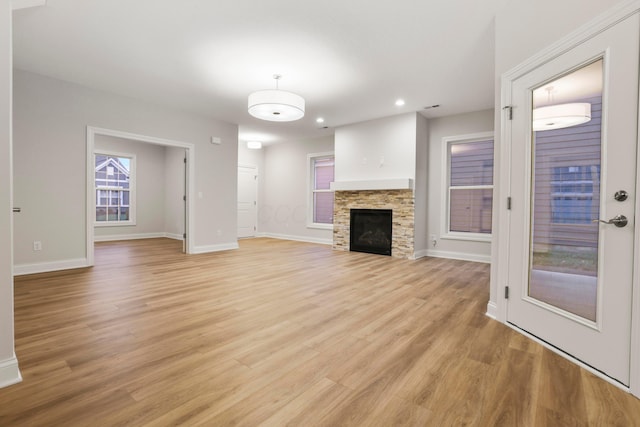 unfurnished living room with light hardwood / wood-style floors and a stone fireplace