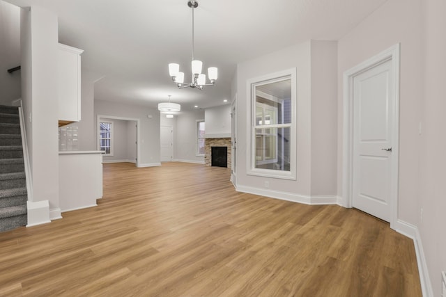 unfurnished living room featuring a stone fireplace, light wood-type flooring, and a chandelier