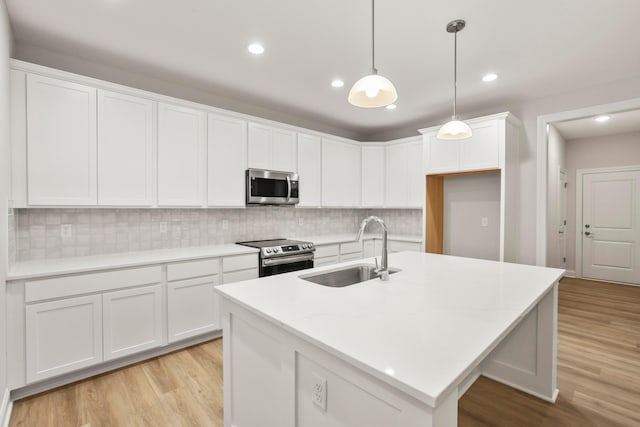 kitchen featuring a center island with sink, sink, decorative light fixtures, white cabinetry, and stainless steel appliances