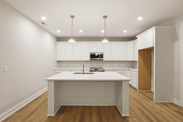 kitchen with sink, stainless steel appliances, pendant lighting, a kitchen island with sink, and white cabinets