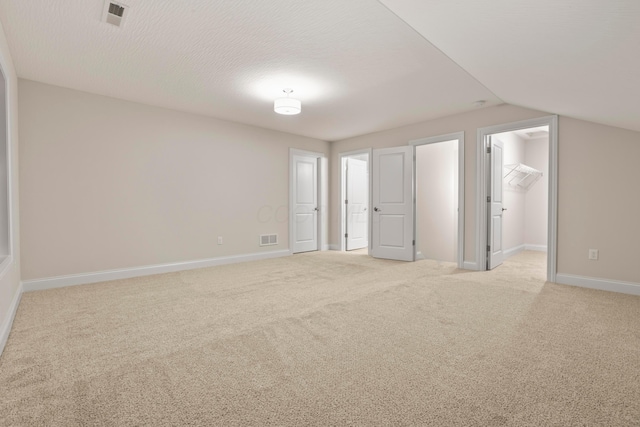 interior space with vaulted ceiling, a spacious closet, a textured ceiling, light colored carpet, and a closet