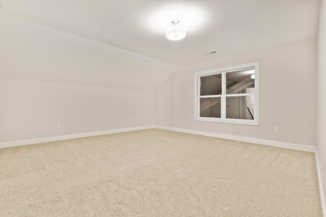 unfurnished room with a textured ceiling, carpet floors, and vaulted ceiling