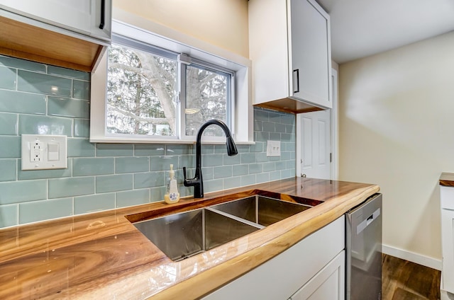 kitchen featuring wooden counters, sink, stainless steel dishwasher, tasteful backsplash, and white cabinetry