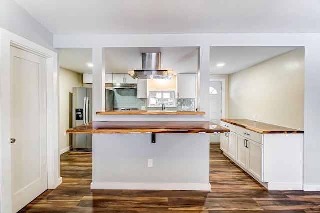 kitchen featuring backsplash, wall chimney exhaust hood, dark wood-type flooring, white cabinets, and butcher block countertops