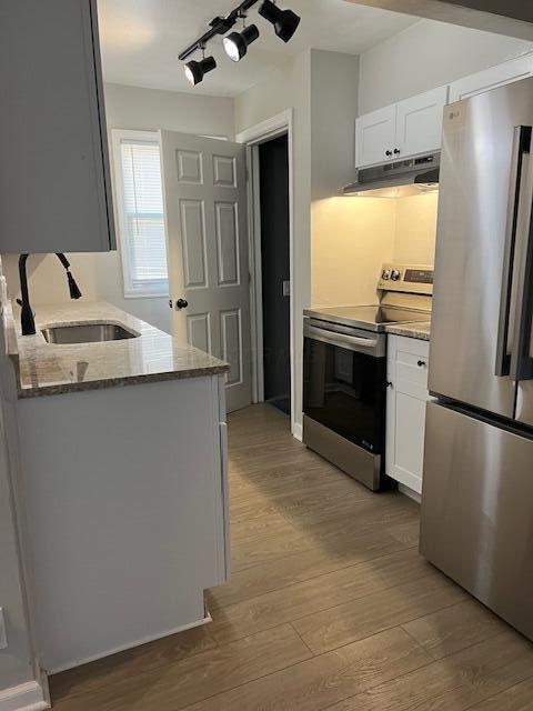 kitchen with sink, light hardwood / wood-style flooring, appliances with stainless steel finishes, white cabinetry, and light stone countertops