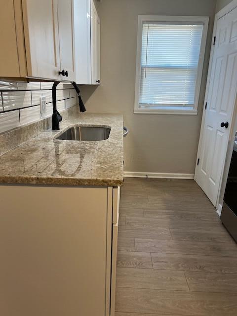 kitchen with white cabinetry, wood-type flooring, sink, and light stone counters