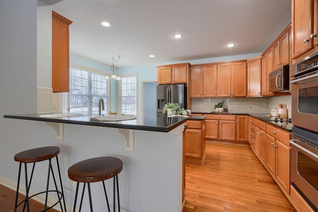 kitchen with stainless steel appliances, a notable chandelier, pendant lighting, a kitchen bar, and light wood-type flooring