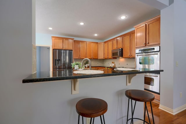 kitchen featuring kitchen peninsula, appliances with stainless steel finishes, tasteful backsplash, hardwood / wood-style flooring, and a breakfast bar area