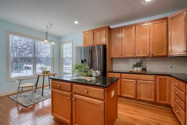 kitchen featuring decorative backsplash, stainless steel fridge, light wood-type flooring, decorative light fixtures, and a kitchen island