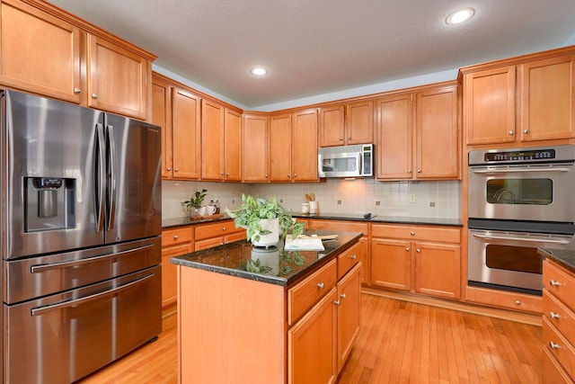 kitchen with stainless steel appliances, backsplash, dark stone countertops, light hardwood / wood-style floors, and a kitchen island