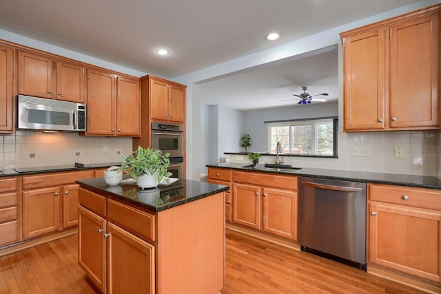 kitchen featuring sink, stainless steel appliances, dark stone counters, light hardwood / wood-style floors, and a kitchen island