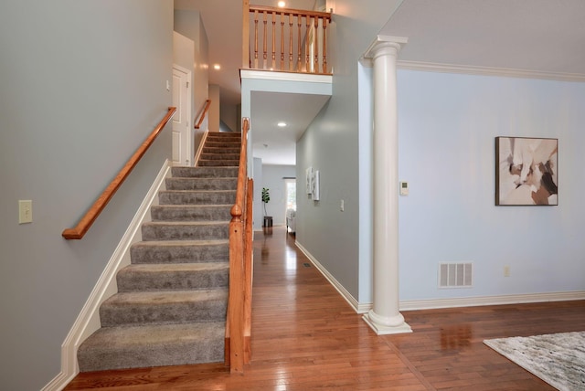 stairs featuring a towering ceiling, decorative columns, hardwood / wood-style flooring, and crown molding