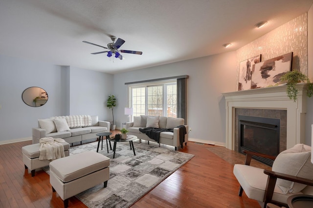 living room featuring hardwood / wood-style flooring, ceiling fan, and a tiled fireplace