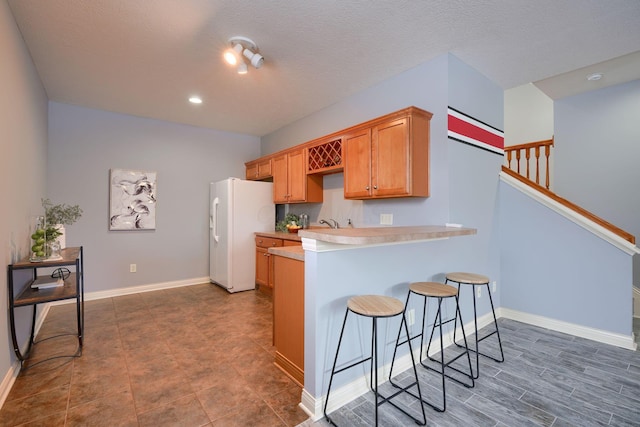 kitchen featuring a textured ceiling, a kitchen breakfast bar, white refrigerator with ice dispenser, and kitchen peninsula